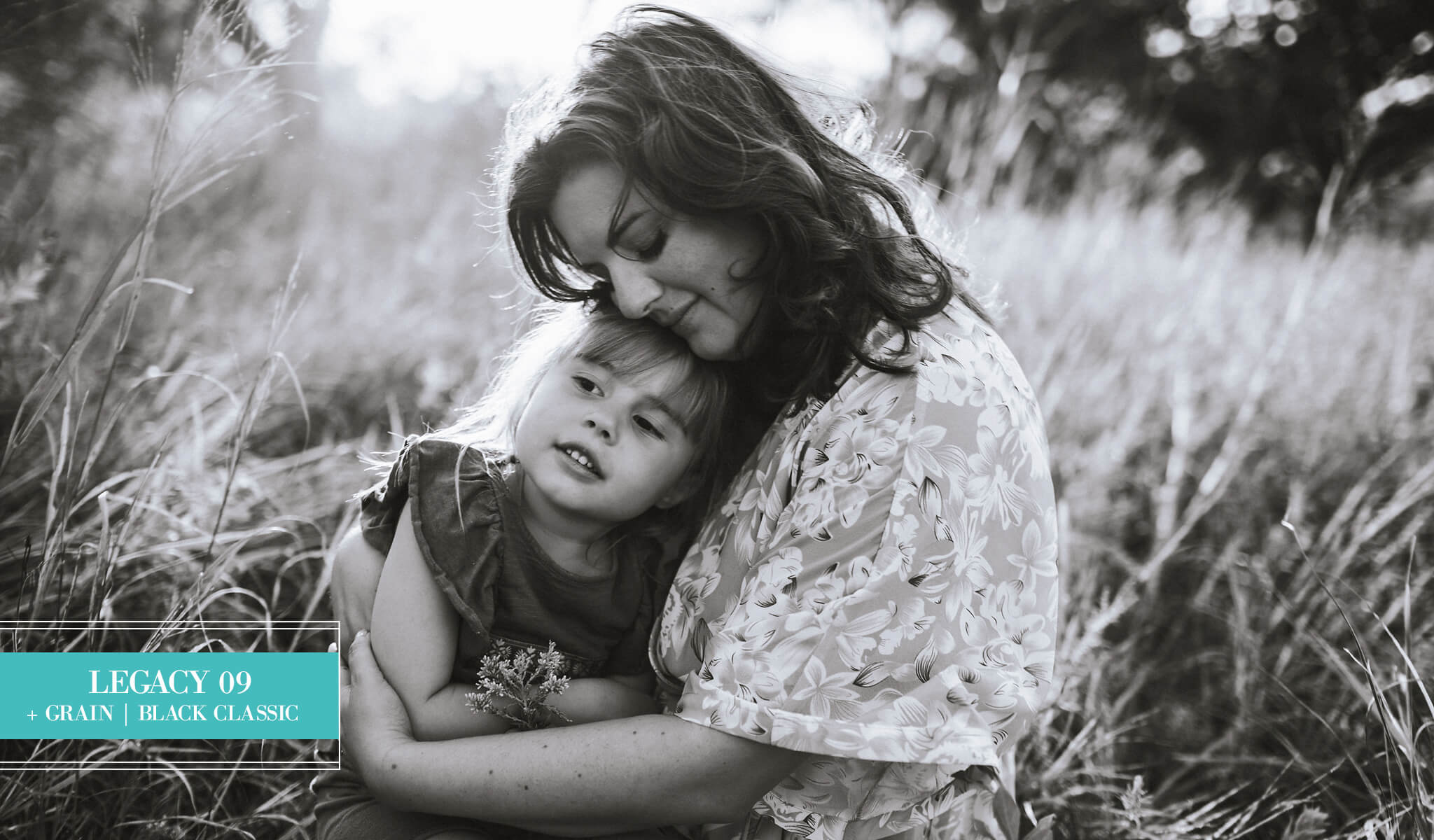 Black and white photograph of a woman hugging a young girl in tall grass outdoors, edited with Legacy Lightroom Presets from Pretty Presets